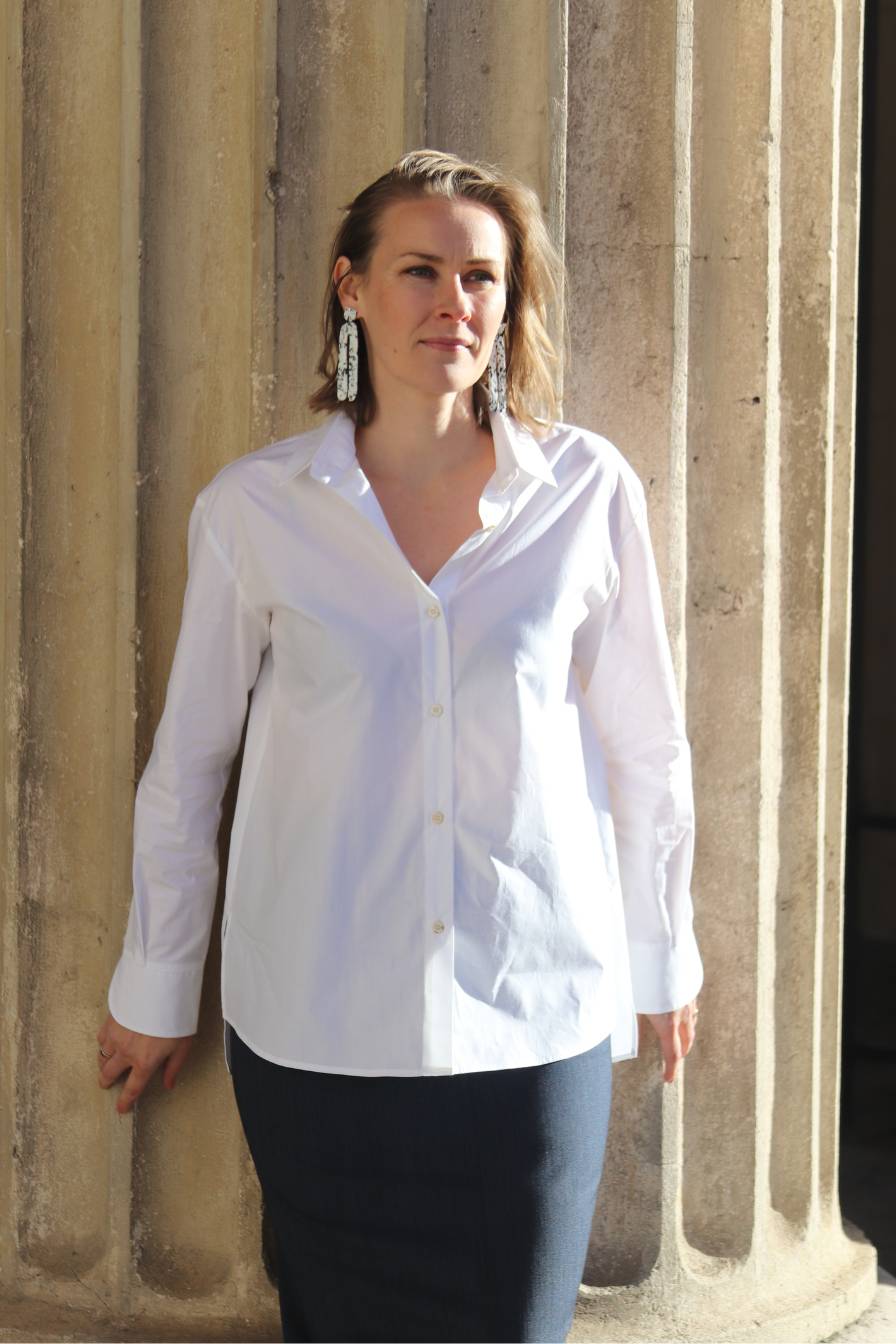 Frau in dunkelblauem Anzugrock mit weißer Hemdbluse vor Säule stehend