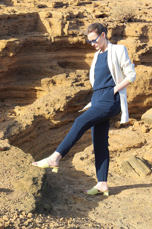 Frau vor Felsenlandschaft in schmalem dunkelblauem Jumpsuit und hellem Blazer aus Bio Leinen