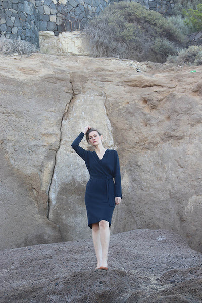 Frau in dunkelblauem knielangem Kleid auf Felsen stehend