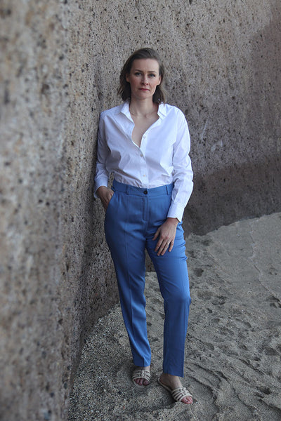 Frau in kornblauer Anzughose und weißem Hemd am Strand