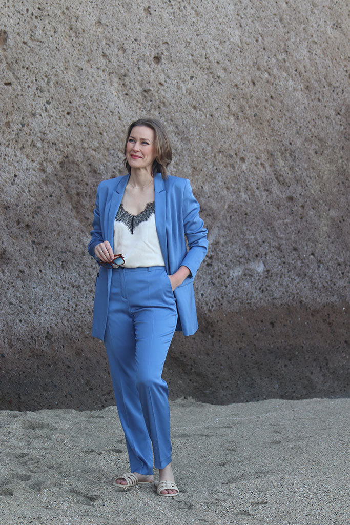 Frau in Kornblauem Anzug und Spitzentop am Strand stehend