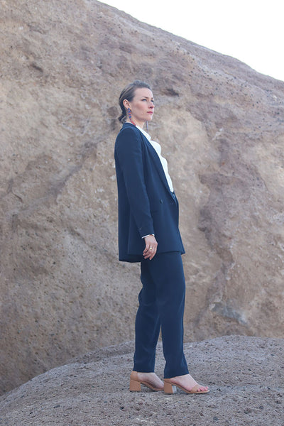 Frau in dunkelblauem Anzug und weißem Hemd auf Felsen stehend