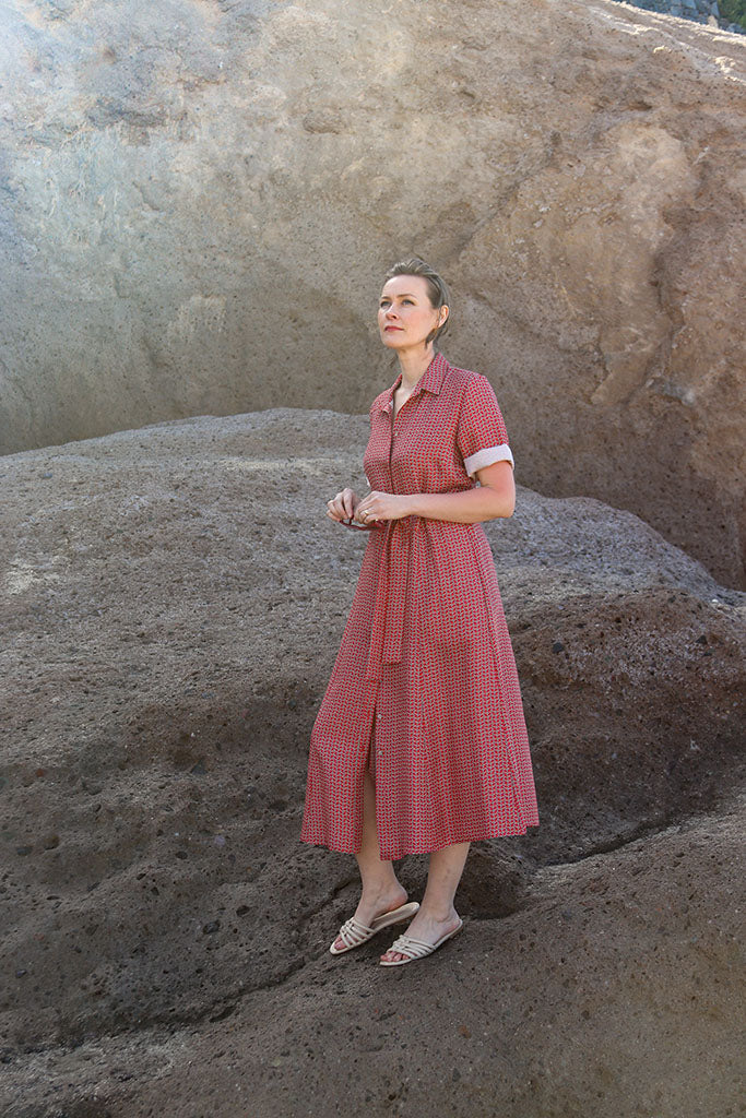Frau in Hemdblusenkleid aus Seide rot gemustert auf Felsen stehend