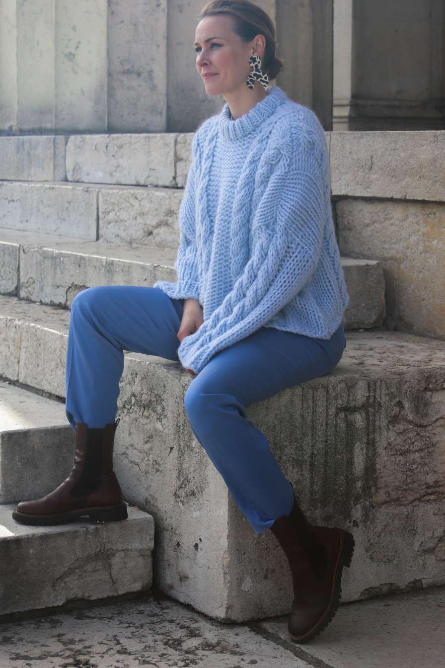 Frau in kornblauer Anzughose und hellblauem Strickpullover auf Treppe sitzend 