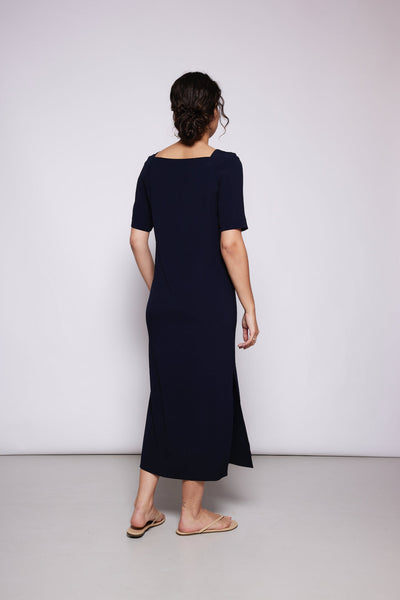 Rückenansicht Frau in dunkelblauem Kleid vor weißer Wand